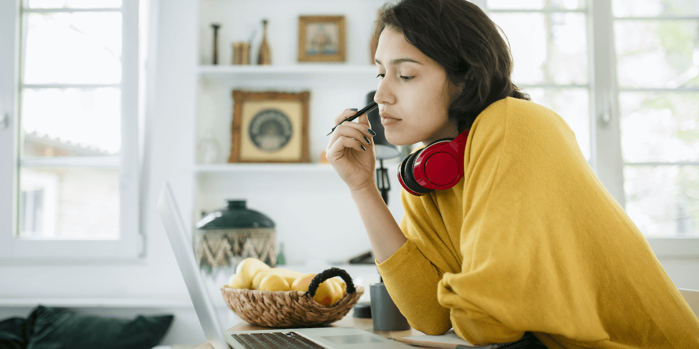 person sitting at home looking at their laptop and holding a pen