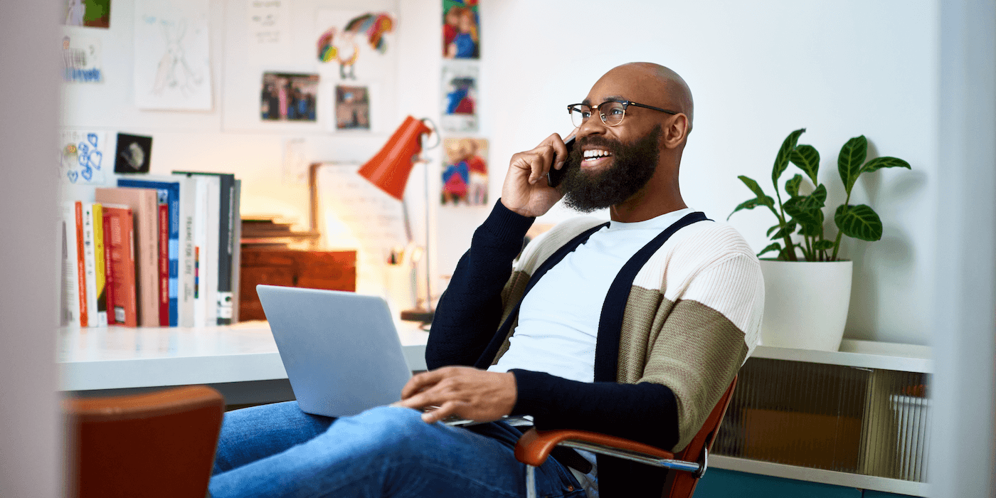 person sitting in home office with laptop on their lap and talking on the phone