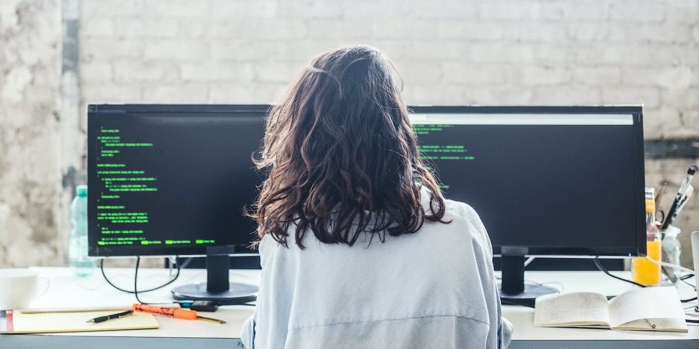 person sitting in front of two computer screens and writing code