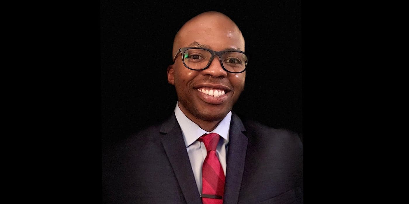 smiling person wearing glasses and a suit with a red tie