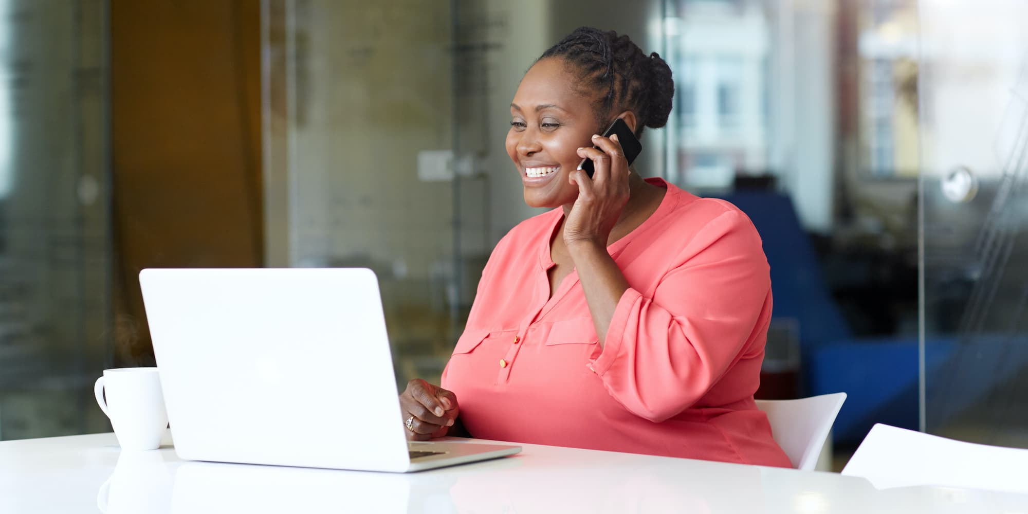 person talking on phone while looking at laptop and sitting alone in conference room