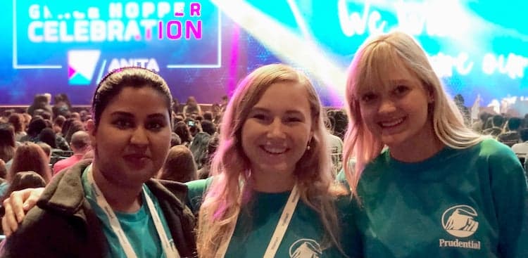 3 women wearing Prudential T-shirts with a sign saying "Grace Hopper Celebration" in the background