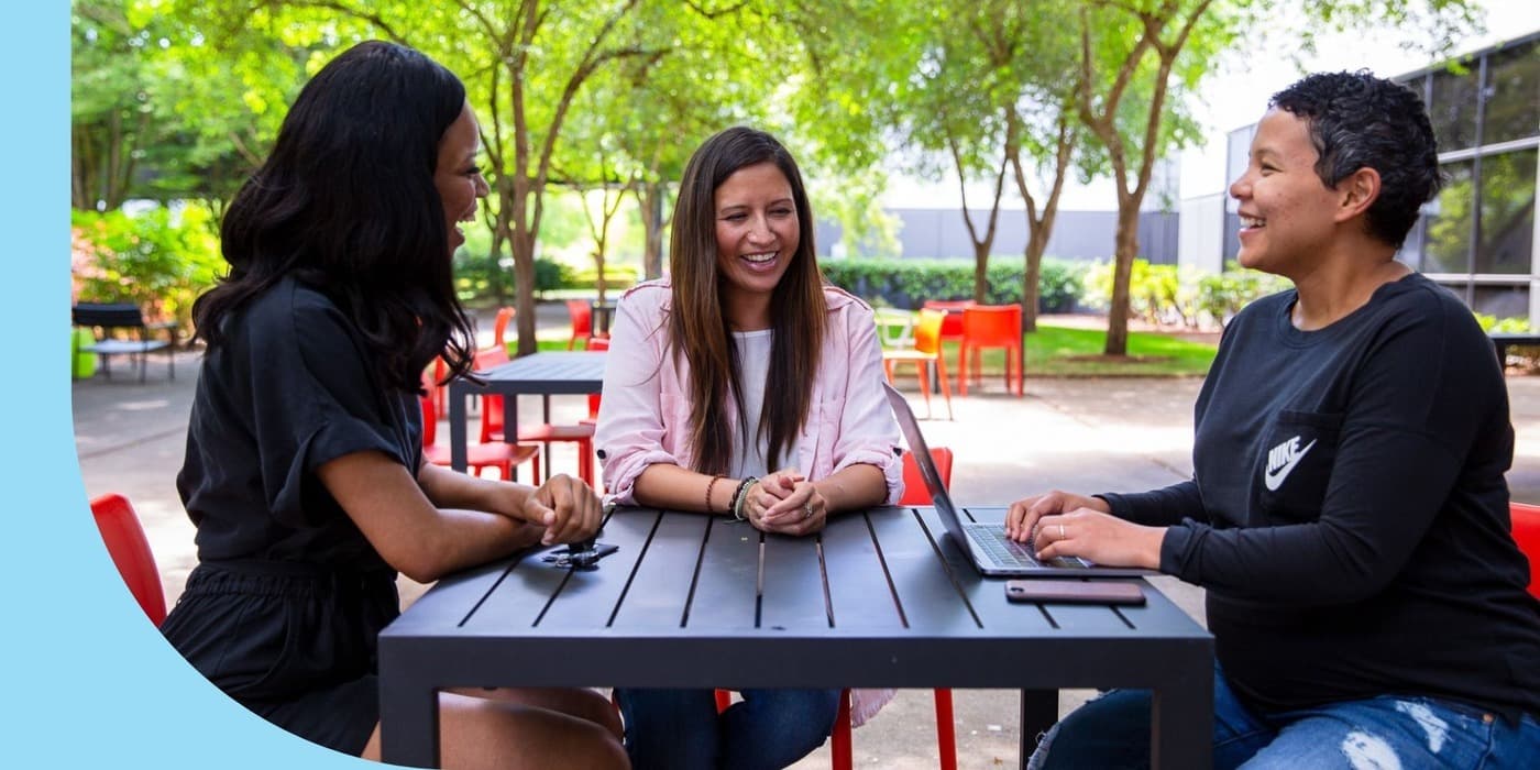 Three NIKE, Inc. employees sitting and talking in an outdoor courtyard at the company’s headquarters.