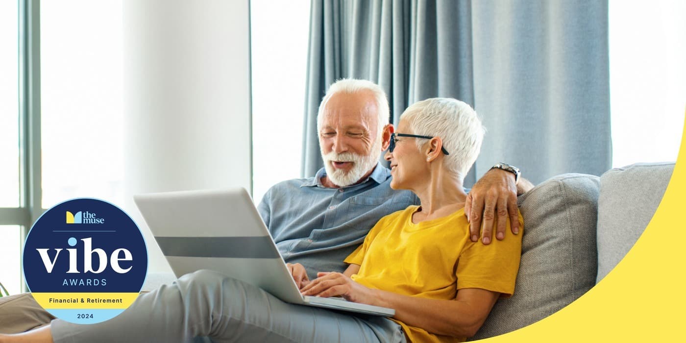 An elderly couple smiling while using a laptop on the couch