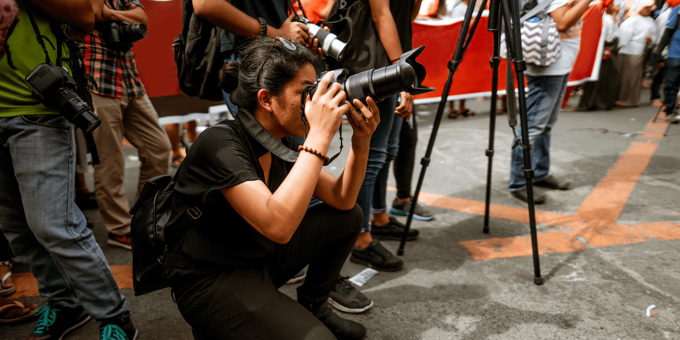 photojournalist crouching down and pointing their camera as other photographers stand nearby