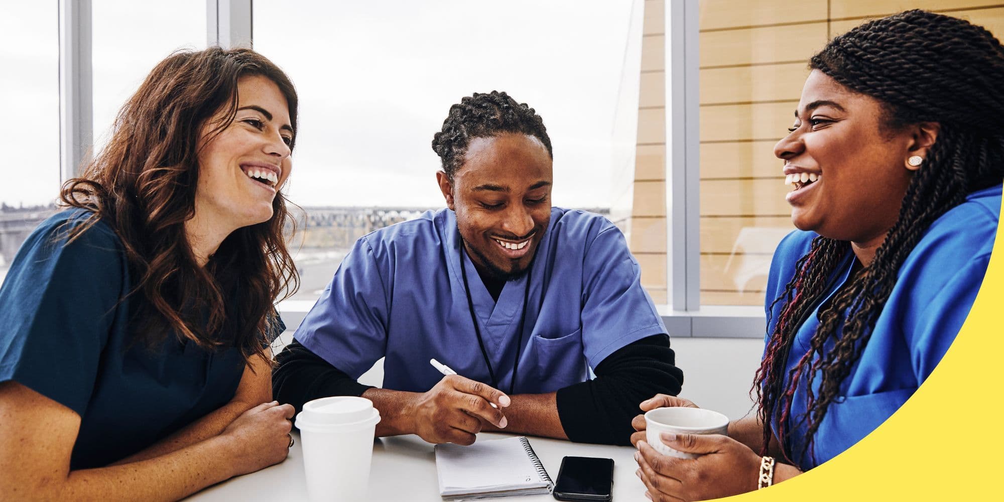 group of coworkers in scrubs sitting around a table laughing with windows in the background